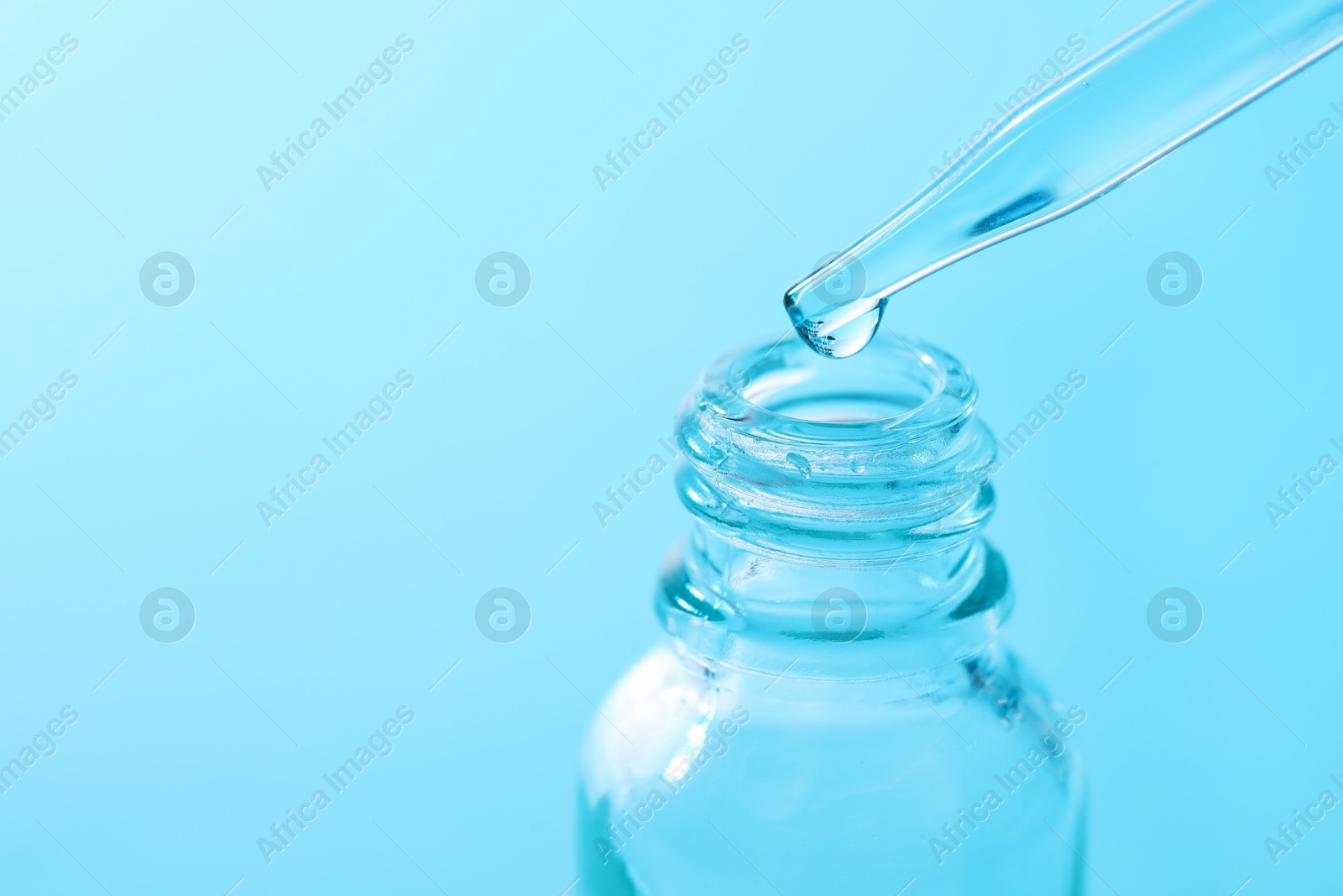 Photo of Dripping liquid from pipette into glass bottle on light blue background, closeup. Space for text