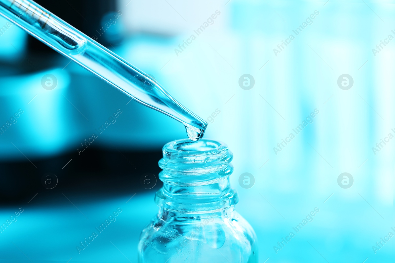 Photo of Dripping liquid from pipette into glass bottle on light blue background, closeup