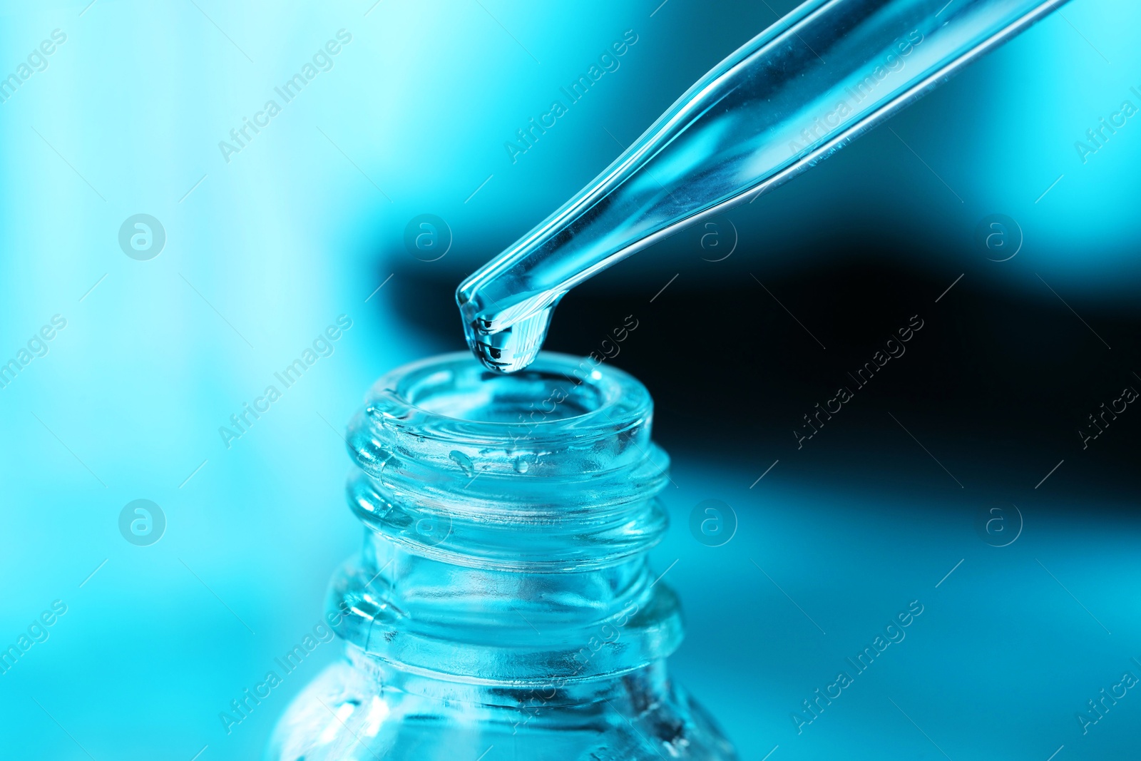 Photo of Dripping liquid from pipette into glass bottle on light blue background, closeup