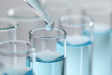 Dripping liquid from pipette into test tube on light background, closeup