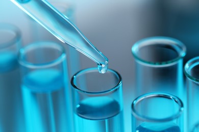 Photo of Dripping liquid from pipette into test tube on blurred background, closeup