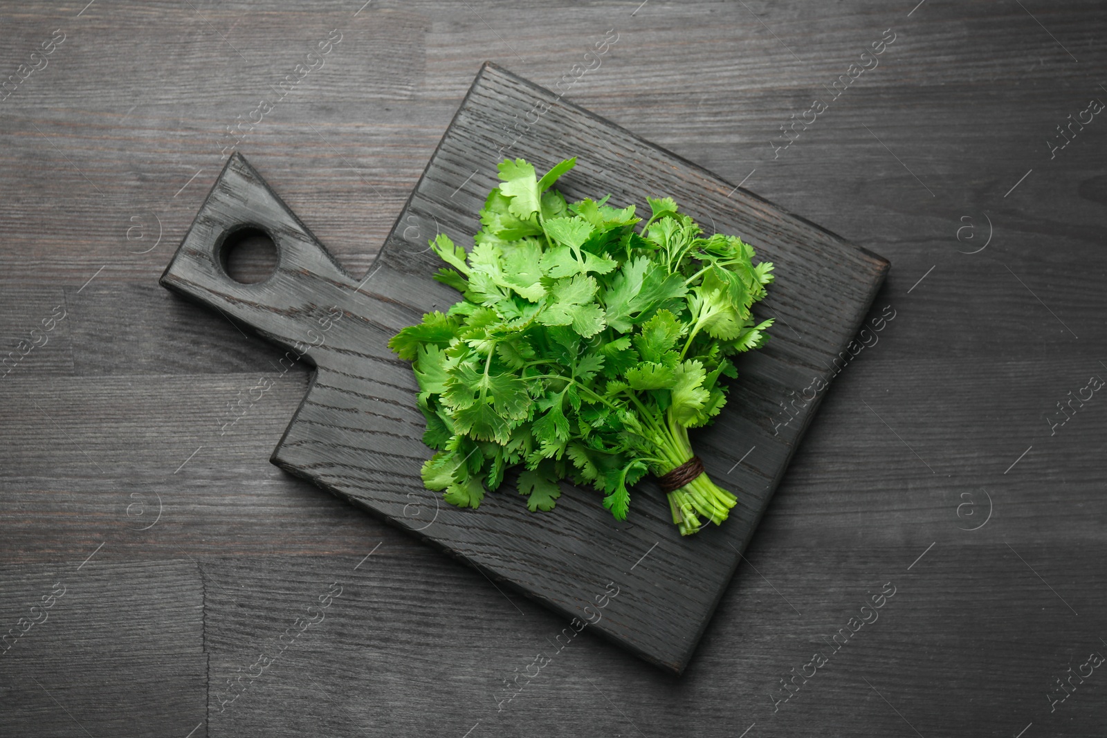 Photo of Bunch of fresh coriander on black wooden table, top view