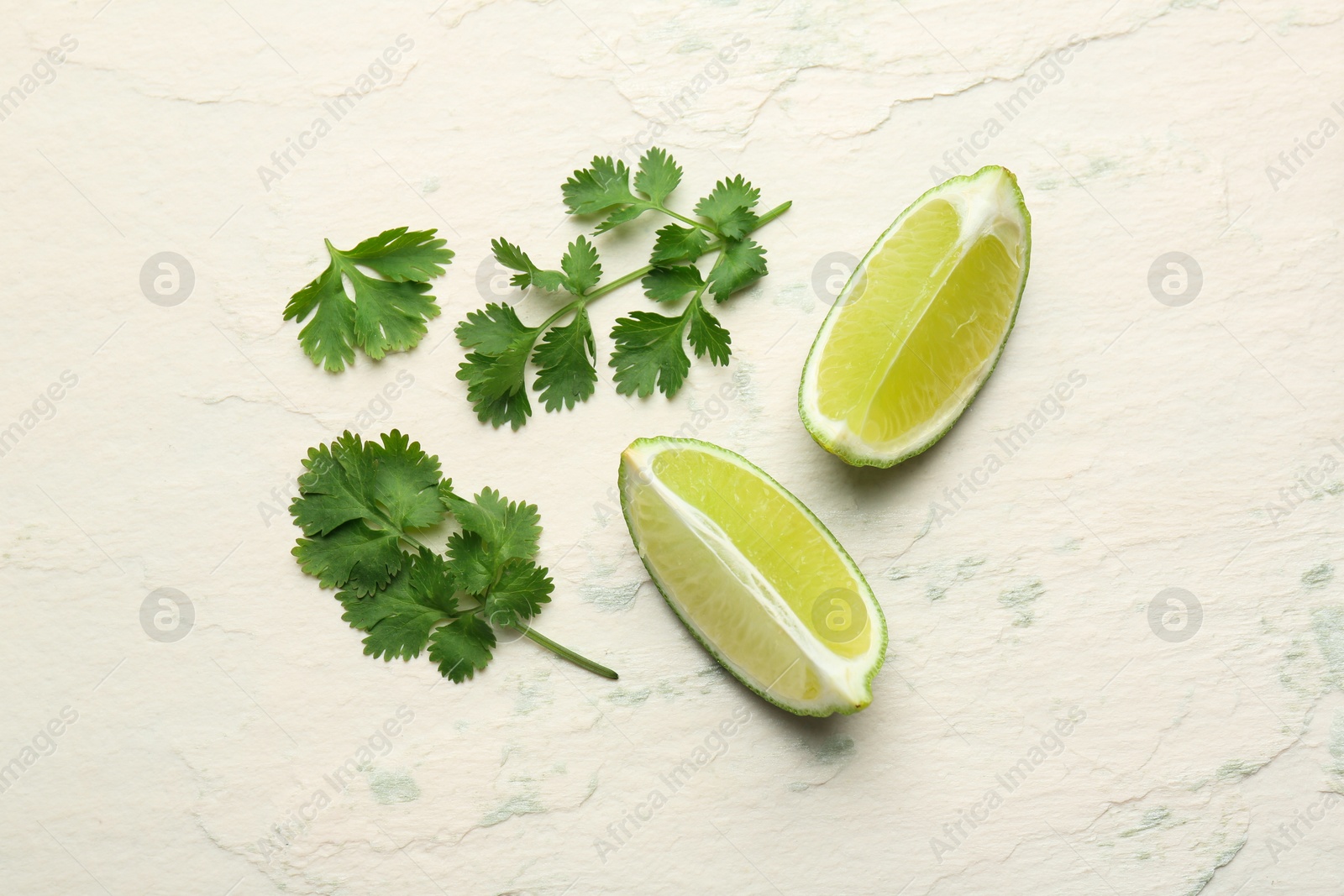 Photo of Fresh coriander leaves and lime wedges on light textured table, flat lay