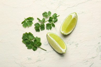 Fresh coriander leaves and lime wedges on light textured table, flat lay