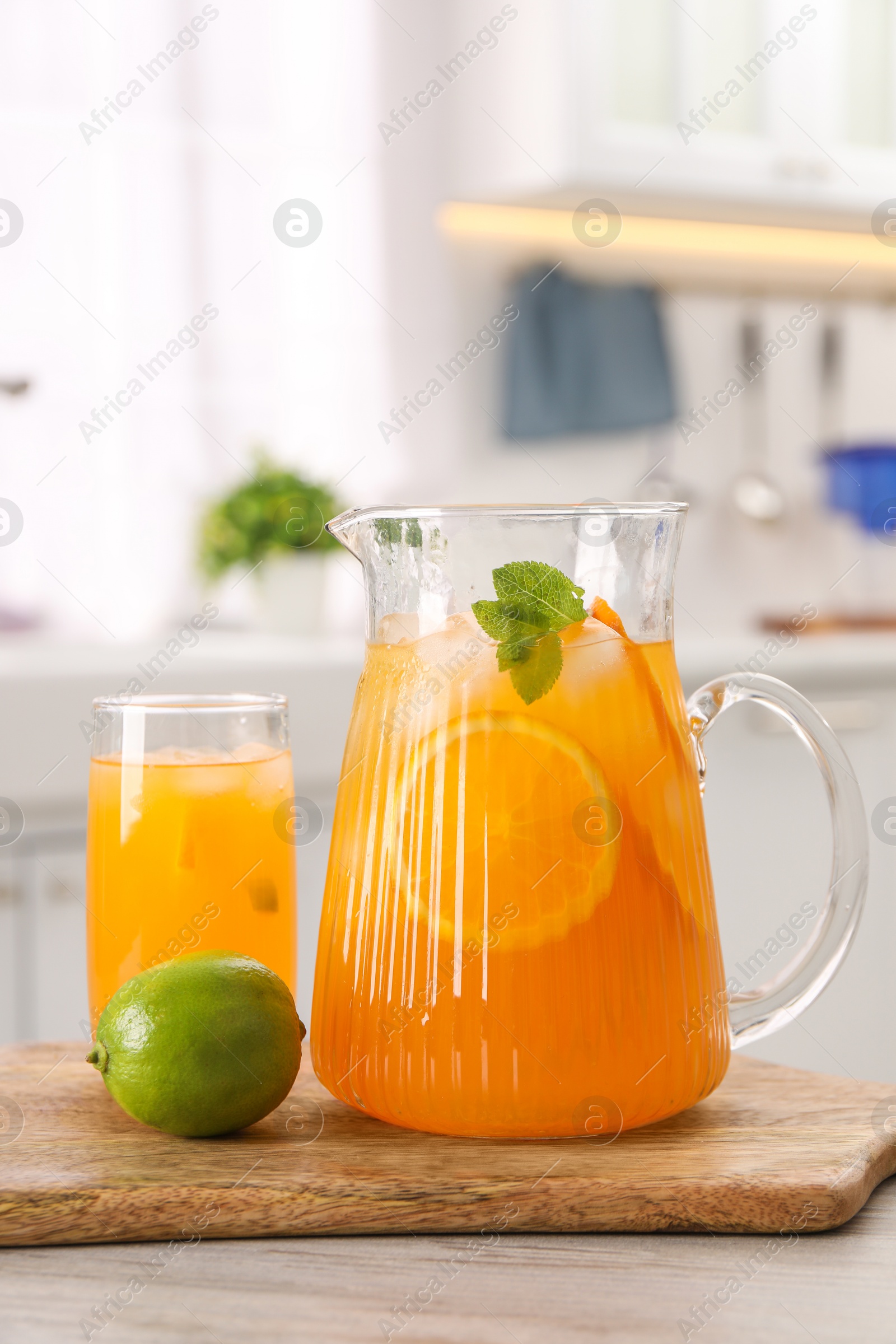 Photo of Tasty lemonade with orange in jug, glass and lime on wooden table in kitchen