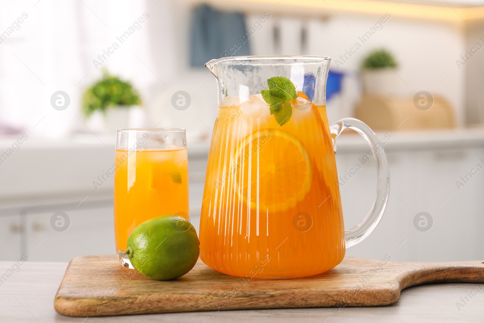 Photo of Tasty lemonade with orange in jug, glass and lime on wooden table in kitchen