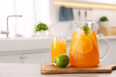 Photo of Tasty lemonade with orange in jug, glass and lime on wooden table in kitchen, space for text