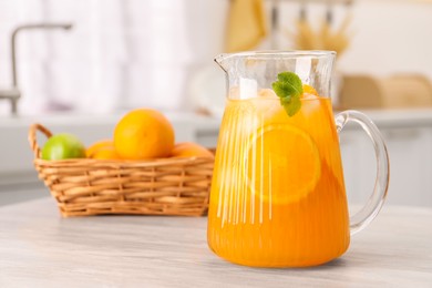 Photo of Freshly made lemonade in jug and citrus fruits on wooden table in kitchen