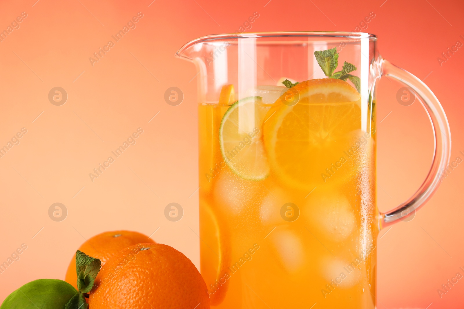 Photo of Freshly made lemonade in jug and citrus fruits against coral background