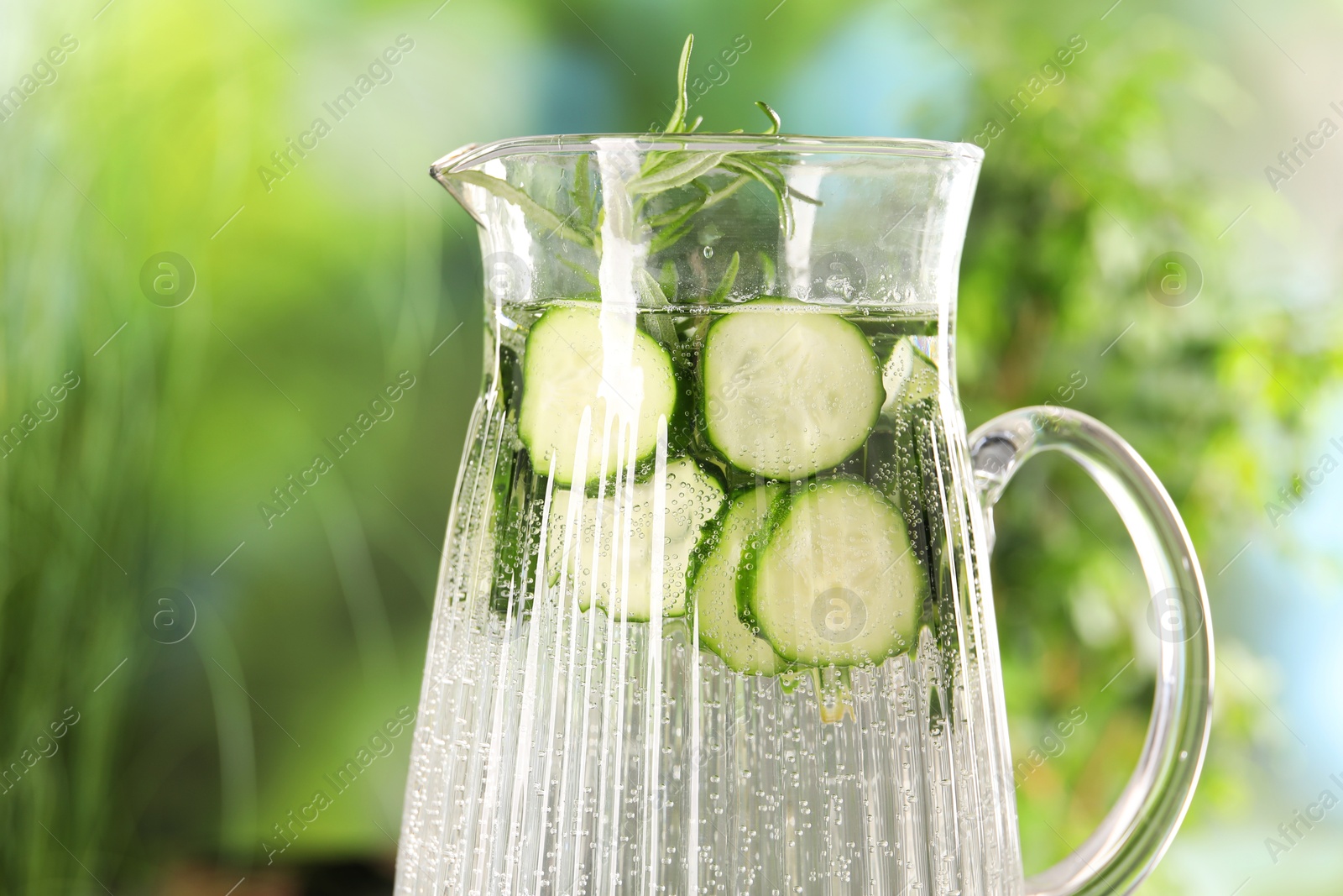 Photo of Refreshing cucumber water with rosemary in jug against blurred green background, closeup