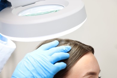 Photo of Trichologist examining patient`s hair under lamp in clinic, closeup