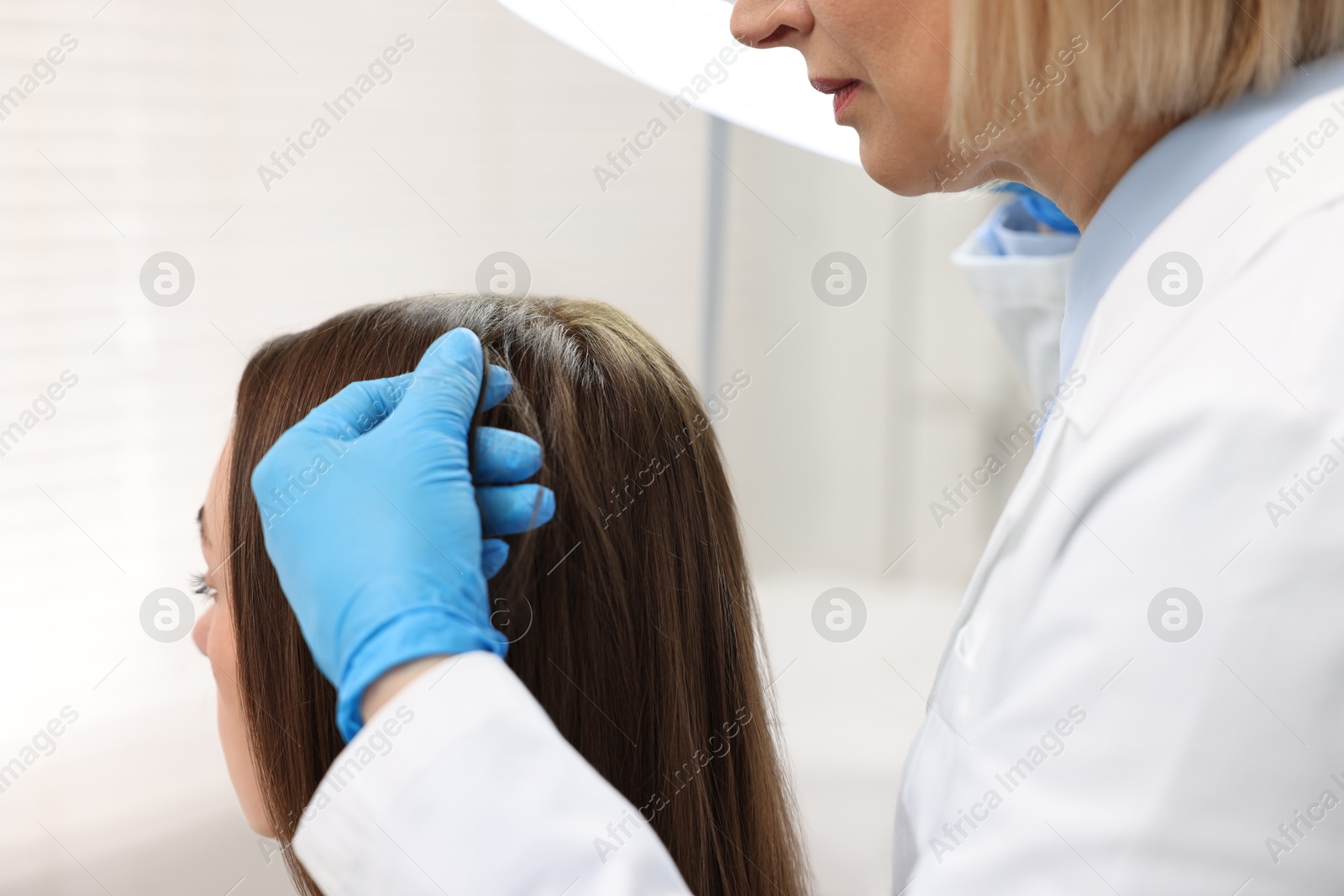 Photo of Trichologist examining patient`s hair under lamp in clinic, closeup