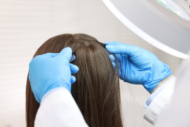 Trichologist examining patient`s hair under lamp in clinic, closeup