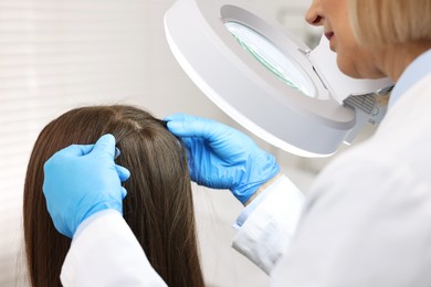 Photo of Trichologist examining patient`s hair under lamp in clinic, closeup