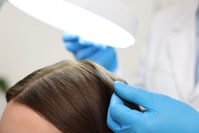 Photo of Trichologist examining patient`s hair under lamp in clinic, closeup