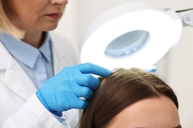 Photo of Trichologist examining patient`s hair under lamp in clinic, closeup