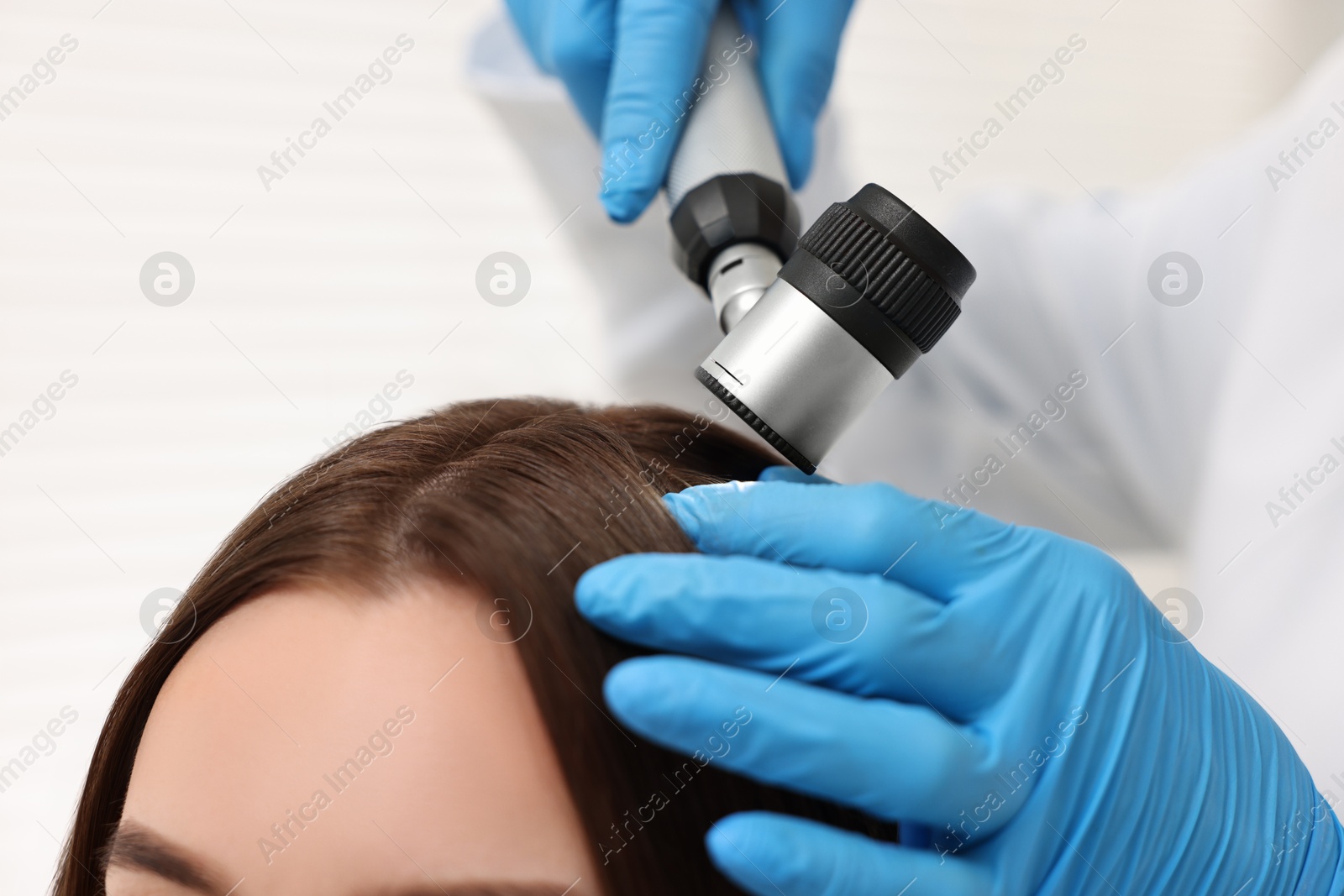 Photo of Trichologist with dermatoscope examining patient`s hair in clinic, closeup