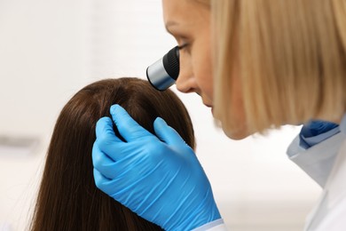 Photo of Trichologist with dermatoscope examining patient`s hair in clinic, closeup