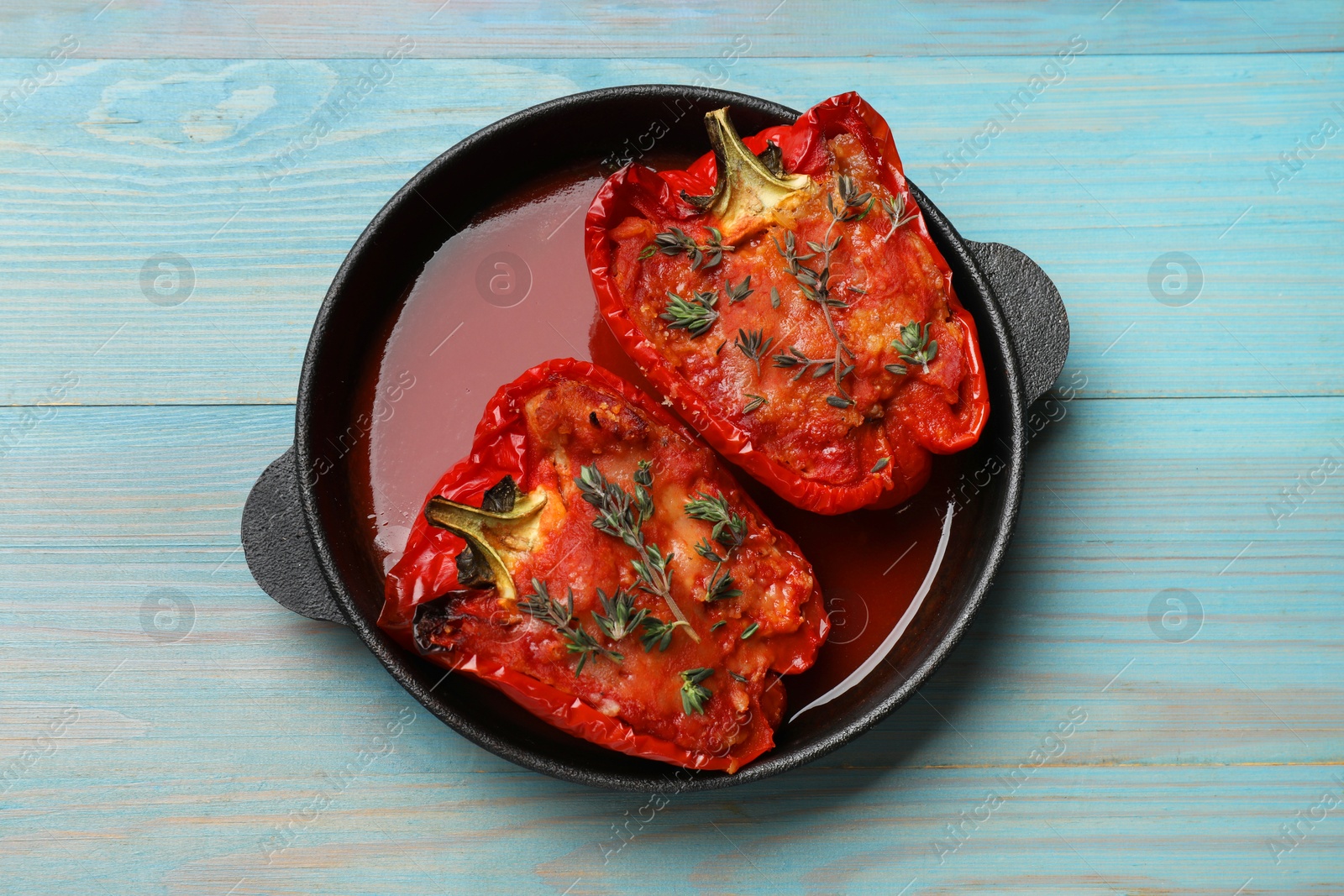 Photo of Tasty stuffed peppers in dish on light blue wooden table, top view