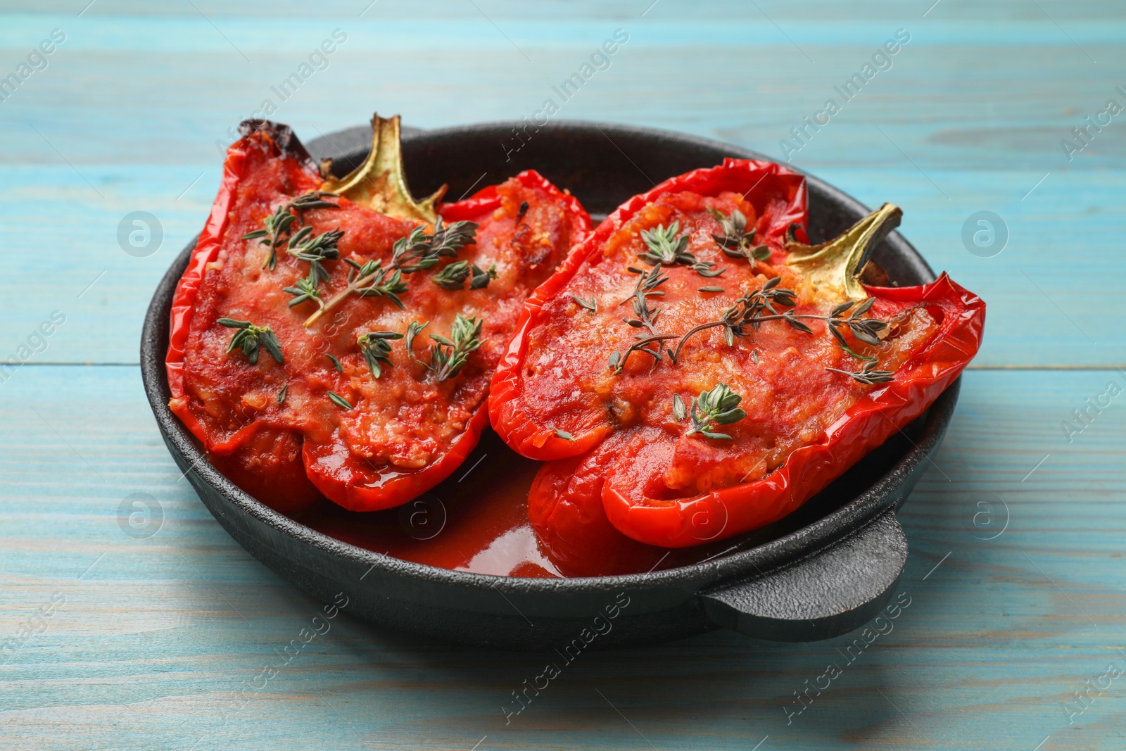 Photo of Tasty stuffed peppers in dish on light blue wooden table