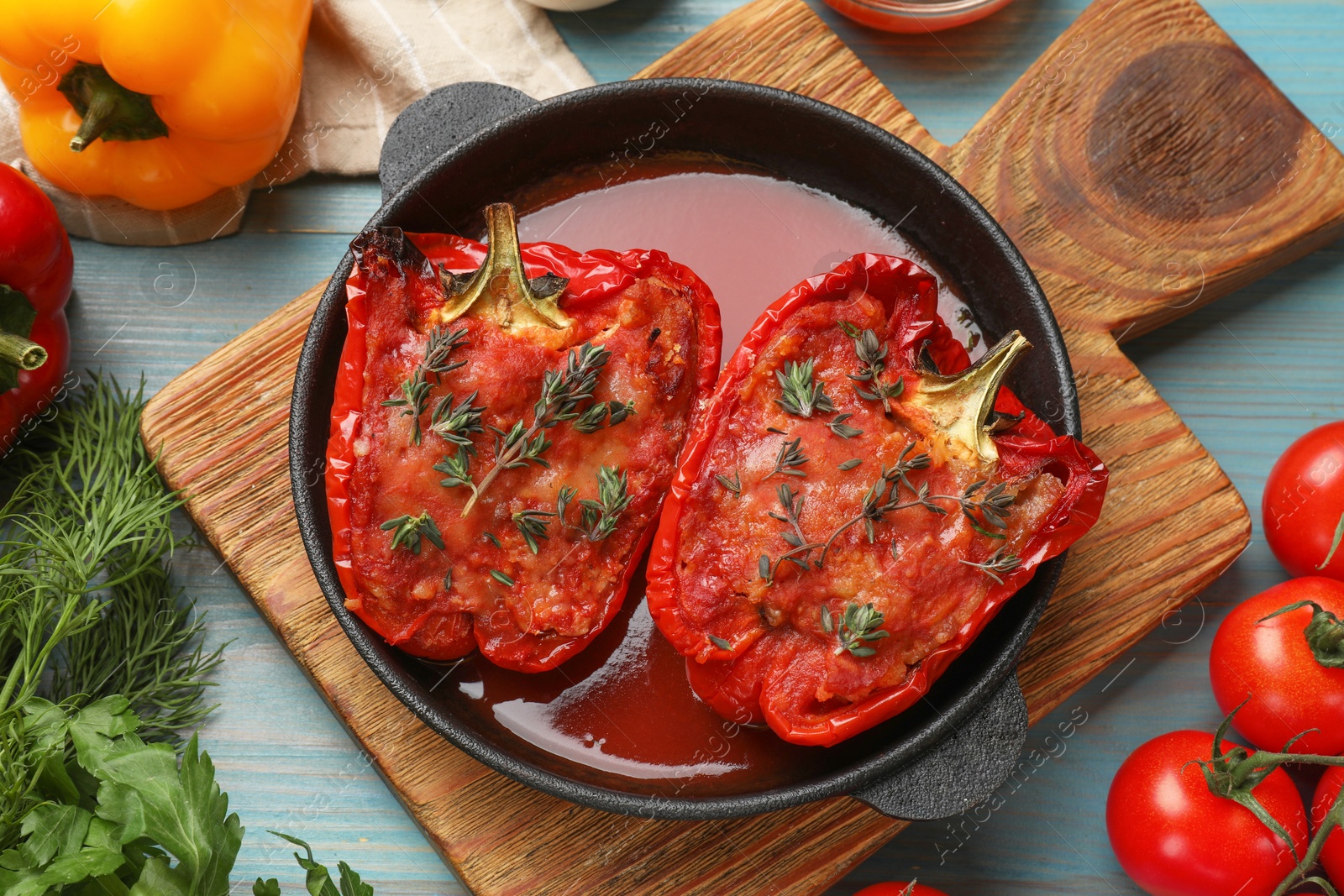 Photo of Tasty stuffed peppers in dish and ingredients on light blue wooden table, flat lay