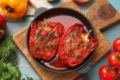 Photo of Tasty stuffed peppers in dish and ingredients on light blue wooden table, flat lay