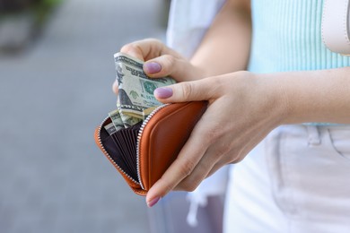 Photo of Woman holding purse with banknotes outdoors, closeup