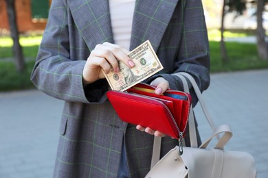 Photo of Woman holding purse with banknotes outdoors, closeup