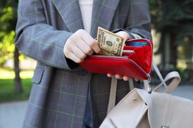 Photo of Woman holding purse with banknotes outdoors, closeup