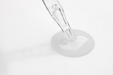 Photo of Glass pipette and transparent liquid on white background, closeup. Space for text