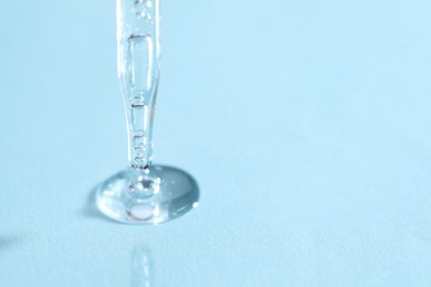 Photo of Glass pipette and transparent liquid on light blue background, closeup. Space for text