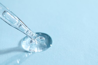 Photo of Glass pipette and transparent liquid on light blue background, closeup. Space for text