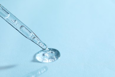 Photo of Glass pipette and transparent liquid on light blue background, closeup. Space for text