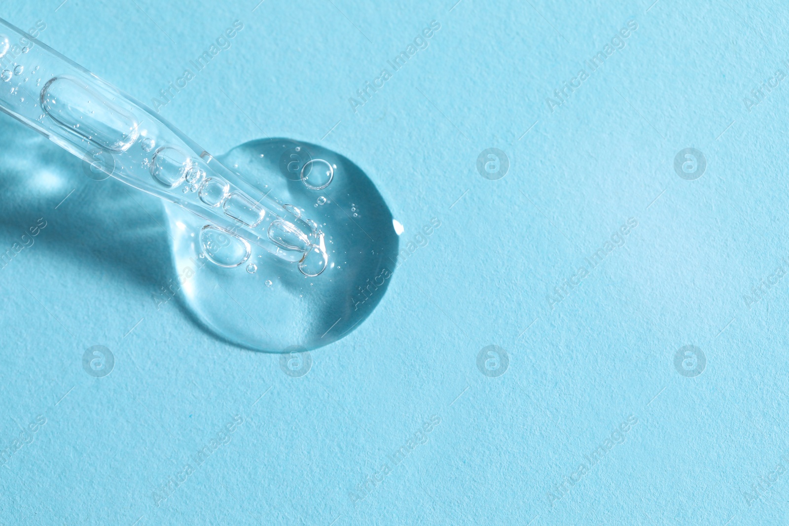 Photo of Glass pipette and transparent liquid on light blue background, top view. Space for text