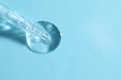Glass pipette and transparent liquid on light blue background, top view. Space for text