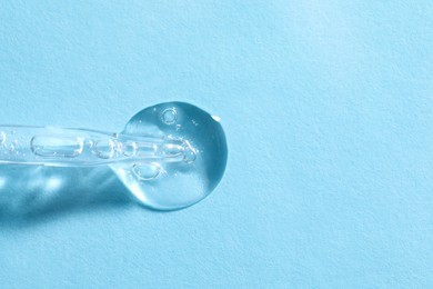 Glass pipette and transparent liquid on light blue background, top view. Space for text