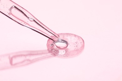 Photo of Glass pipette and transparent liquid on light pink background, closeup