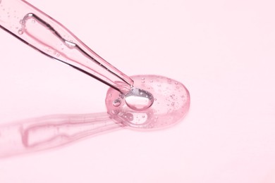 Glass pipette and transparent liquid on light pink background, closeup