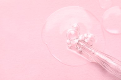 Photo of Glass pipette and transparent liquid on light pink background, top view. Space for text