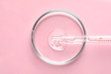 Photo of Glass pipette and petri dish with liquid on pink background, top view