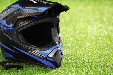 Modern motorcycle helmet with visor on green grass, closeup. Space for text