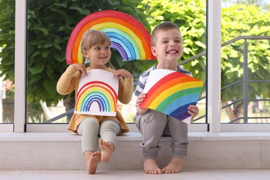 Children with pictures of rainbow near window indoors