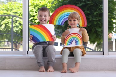 Children with pictures of rainbow near window indoors