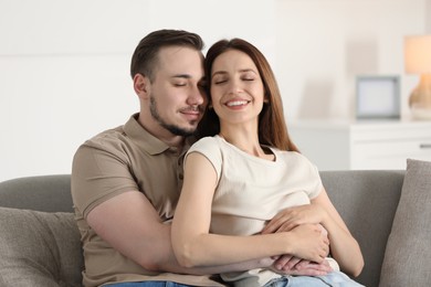 Man hugging his happy girlfriend on sofa at home