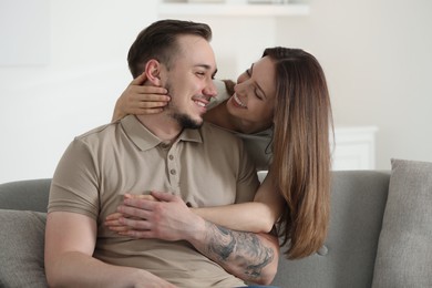 Woman hugging her happy boyfriend on sofa at home