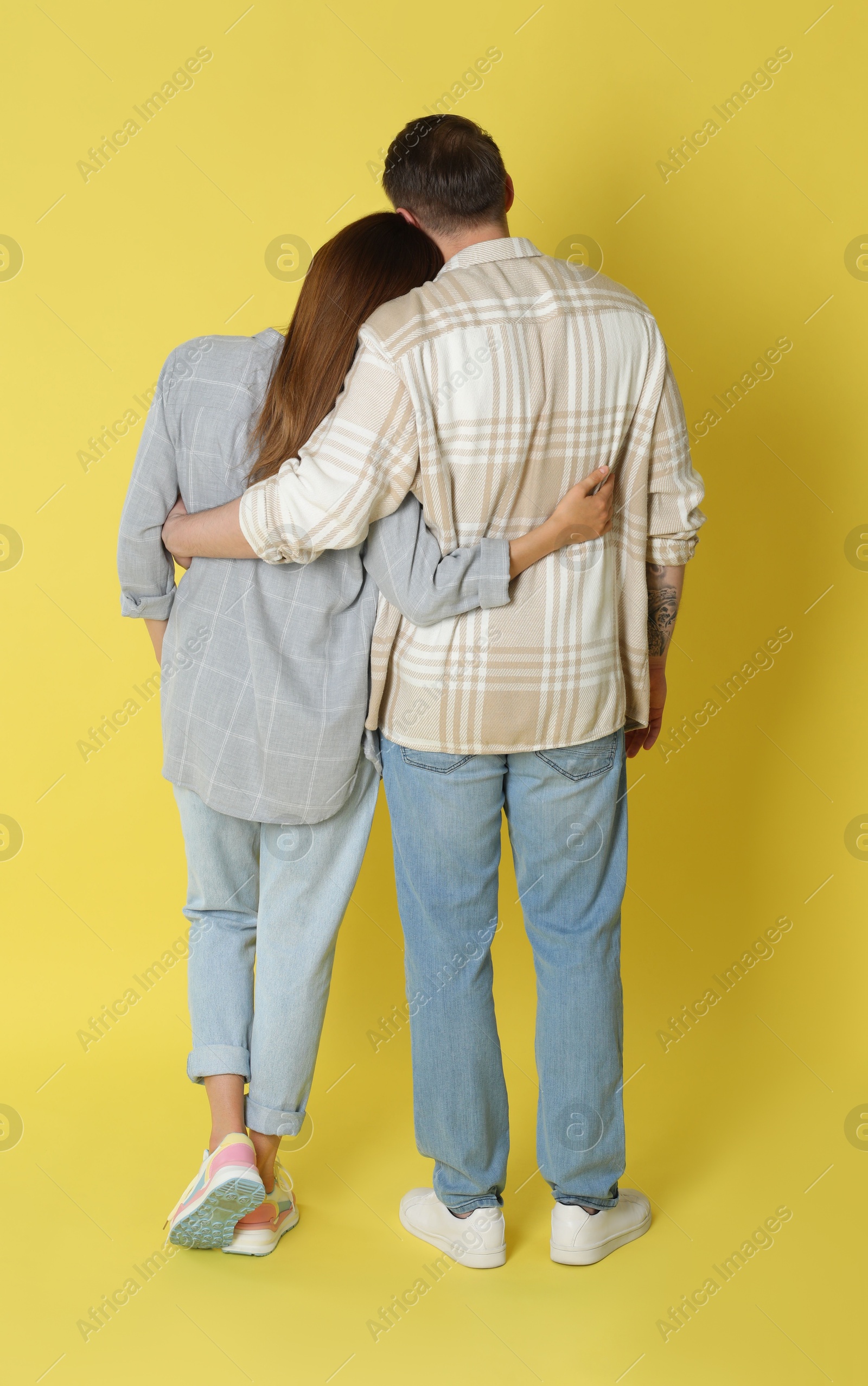 Photo of Cute couple hugging on yellow background, back view