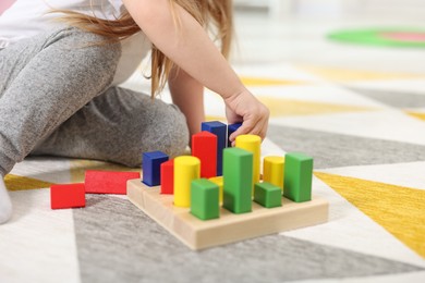 Little girl playing with set of wooden geometric figures on carpet, closeup. Kindergarten activities for motor skills development