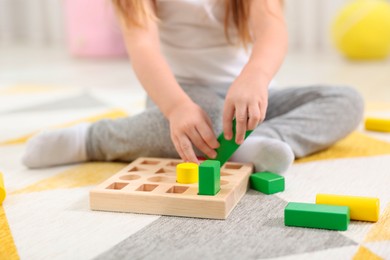 Little girl playing with set of wooden geometric figures on carpet, closeup. Kindergarten activities for motor skills development