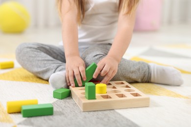 Photo of Little girl playing with set of wooden geometric figures on carpet, closeup. Kindergarten activities for motor skills development