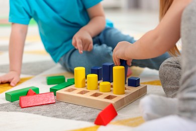 Photo of Little children playing with set of wooden geometric figures on carpet, closeup. Kindergarten activities for motor skills development